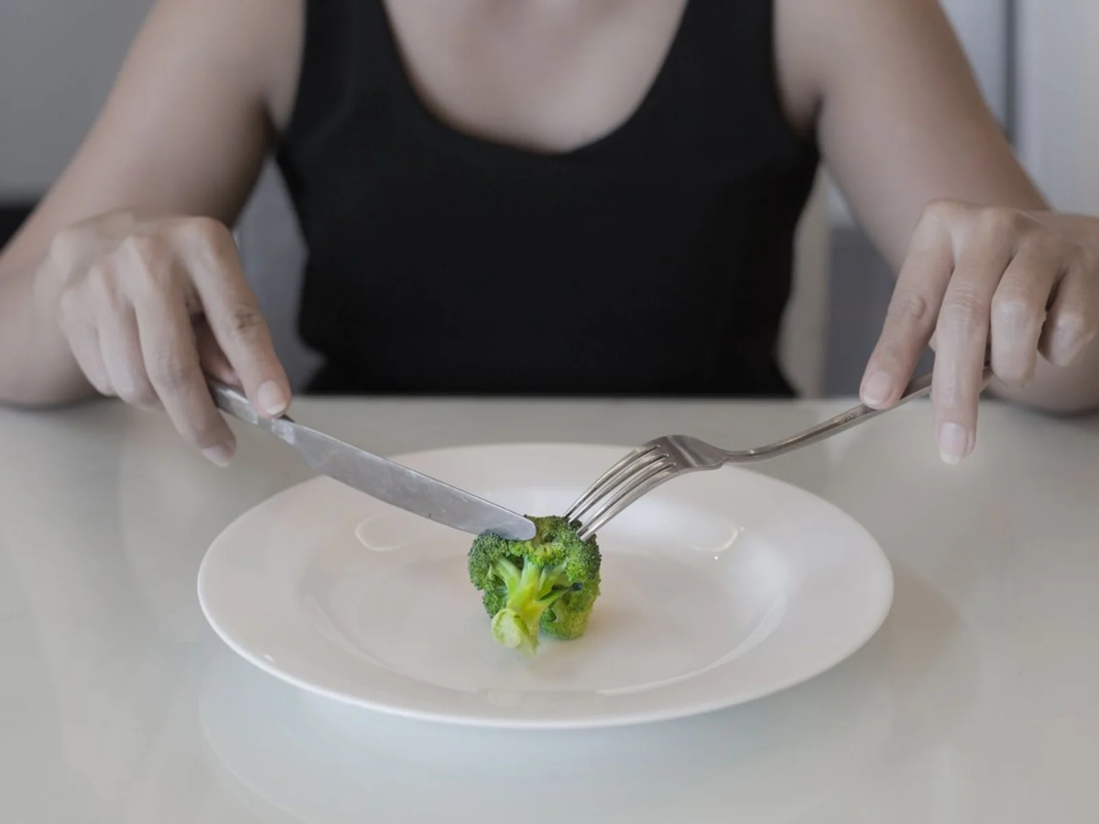 Person eating broccoli on white plate.