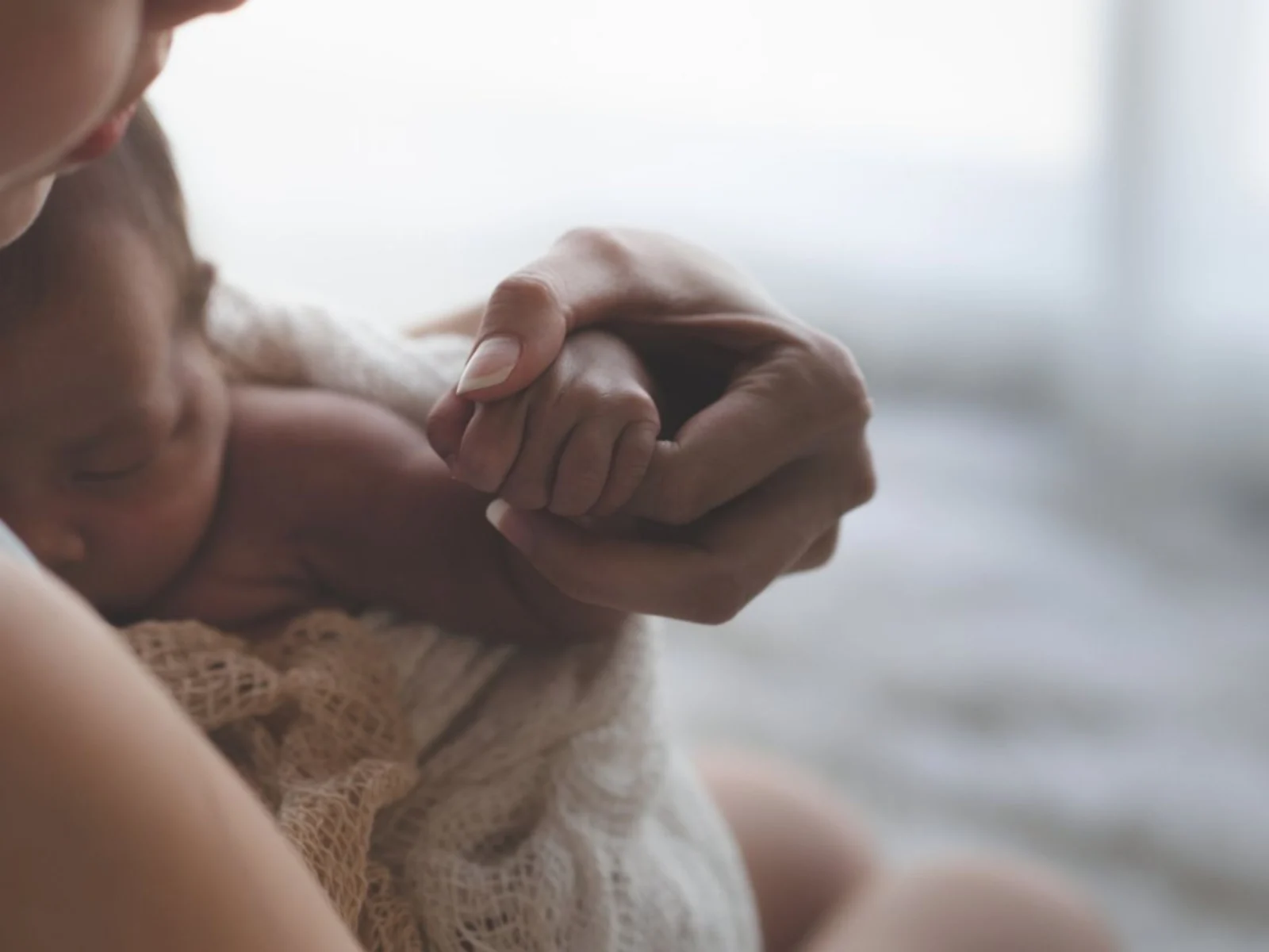 Mother holding newborn's hand, intimacy and connection.
