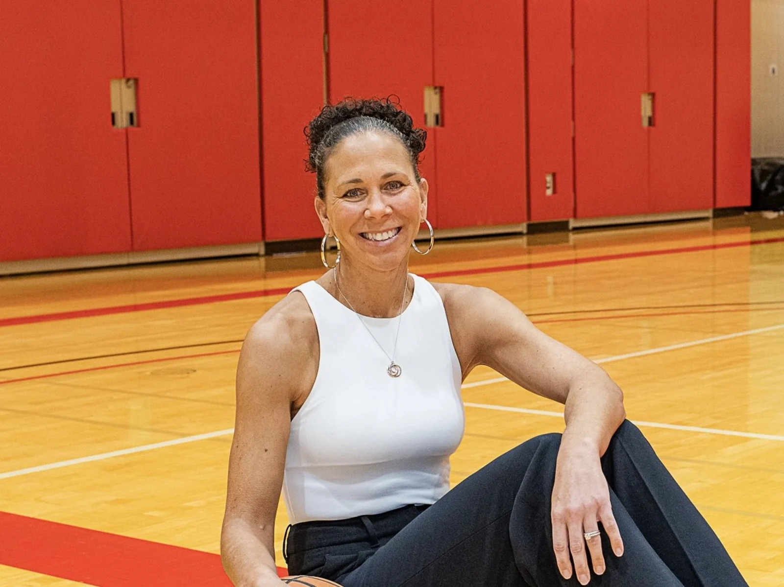 Smiling person on basketball court in white top.