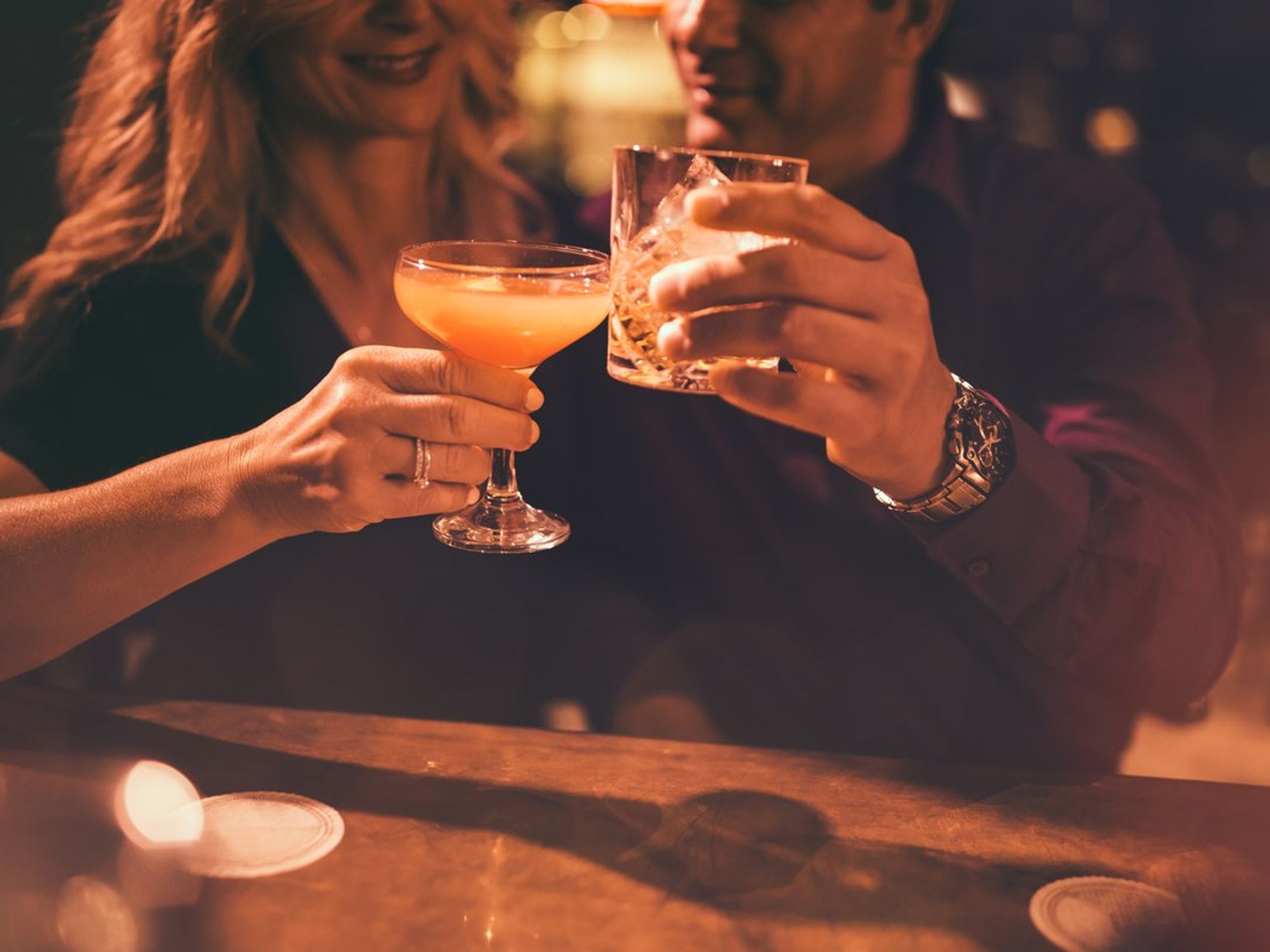 Couple clinking glasses at a dimly lit bar.