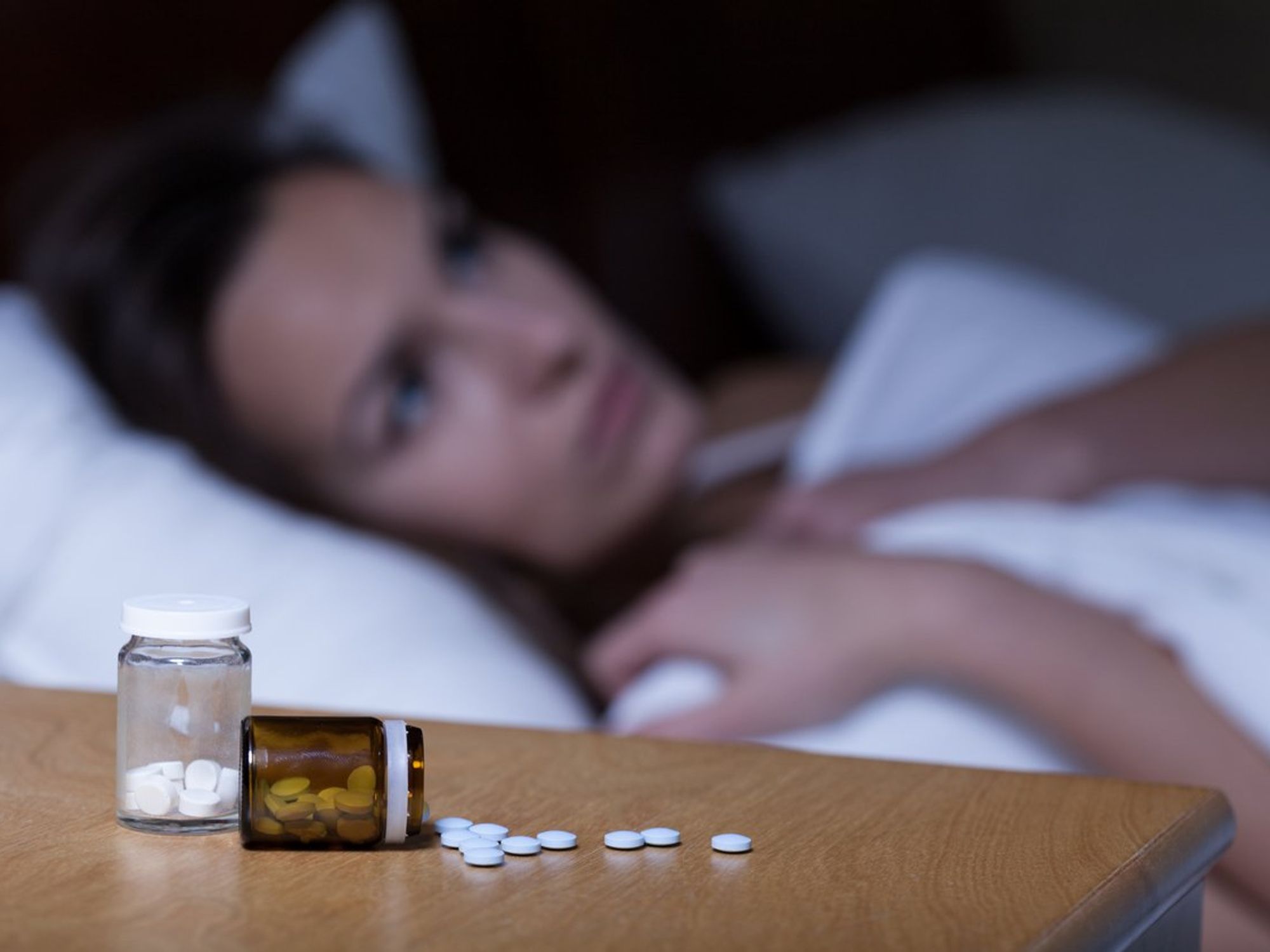Woman lying in bed with pill bottles nearby.