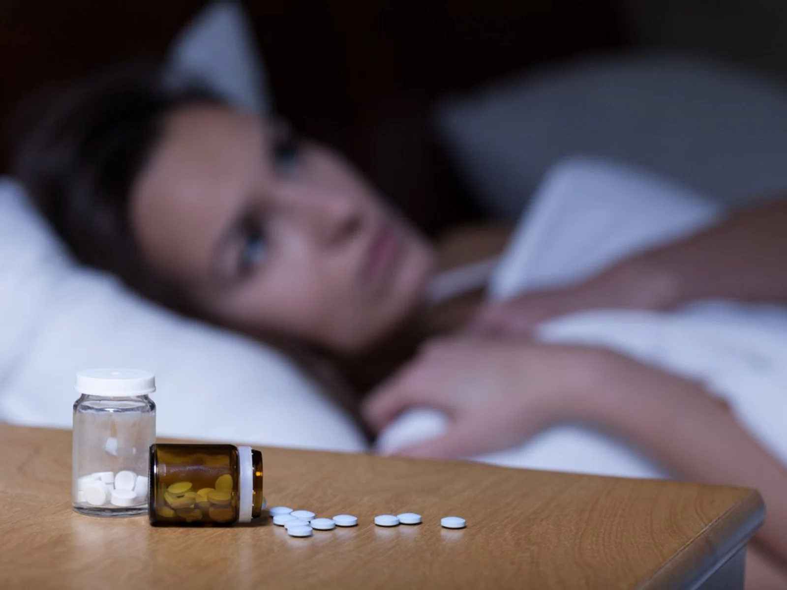 Woman lying in bed with pill bottles nearby.