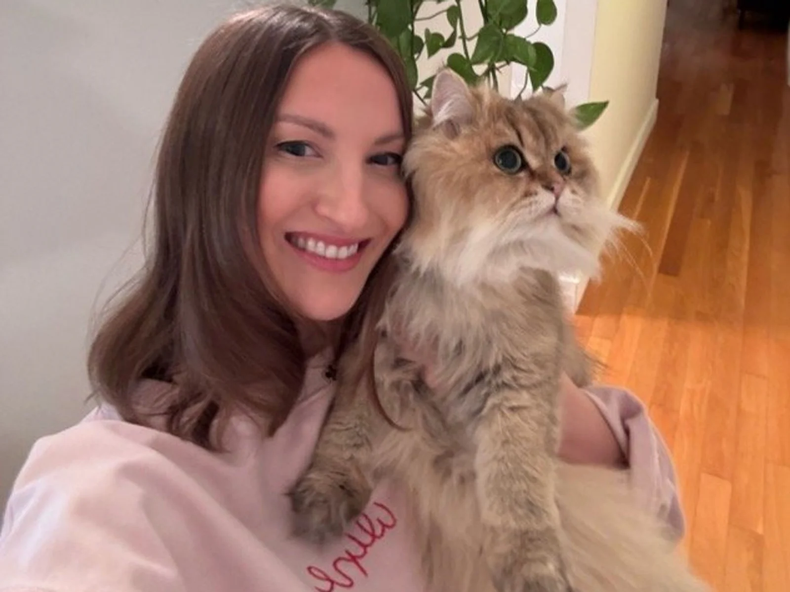 Smiling woman holding fluffy cat indoors.